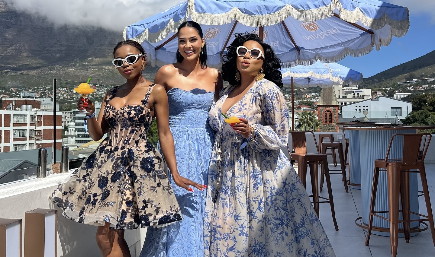 Three women standing together on a sunny rooftop with mountains in the background